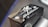 A close-up of a motorcycle part with embossed text and symbols. The text 'Hayabusa' is prominently featured alongside a stylized Japanese character. The part has a metallic, angular design with a black finish and highlights visible on its surface.