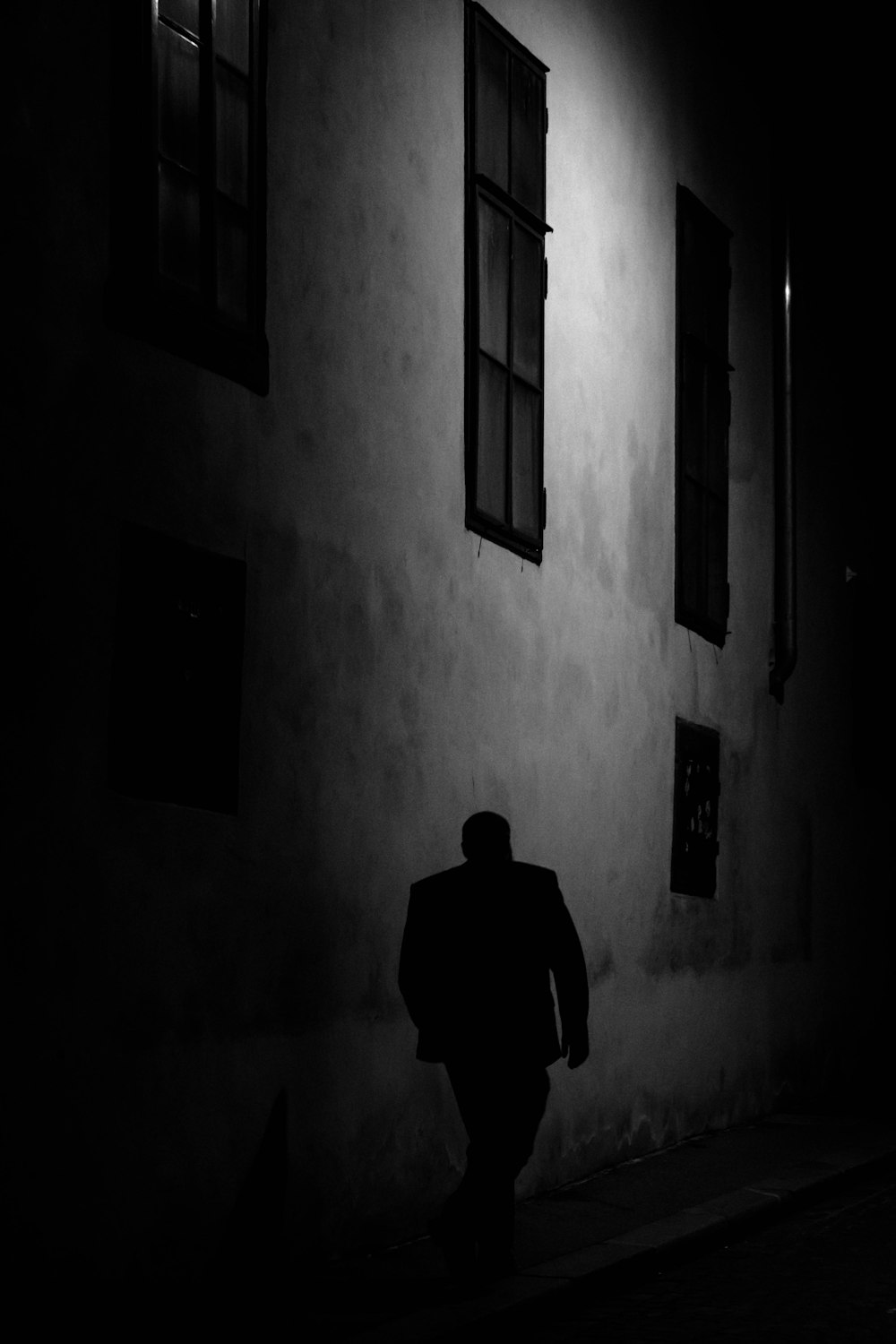 uomo che cammina accanto al muro di cemento grigio durante la notte
