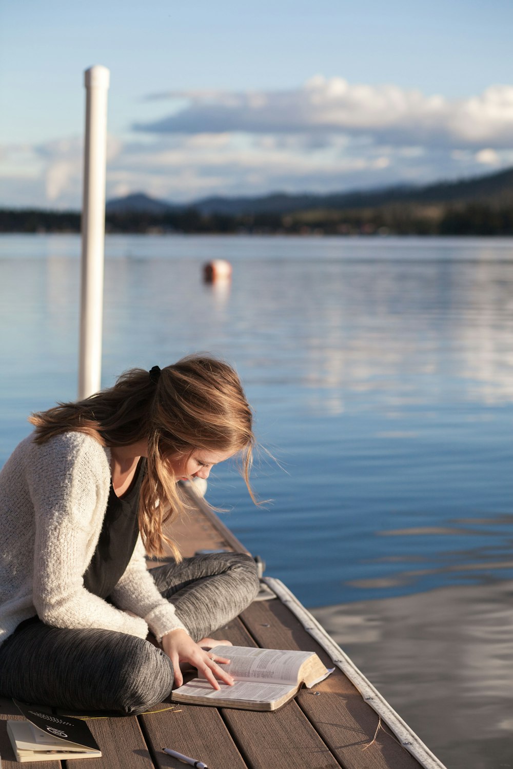 Foto de mujer leyendo un libro cerca del cuerpo de agua