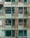 A weathered apartment building facade with visible balconies where laundry is hanging out to dry. The structure has a mix of brickwork and patterned concrete blocks, and the paint is faded. Electrical wires run along the building, and some greenery is visible in planters.