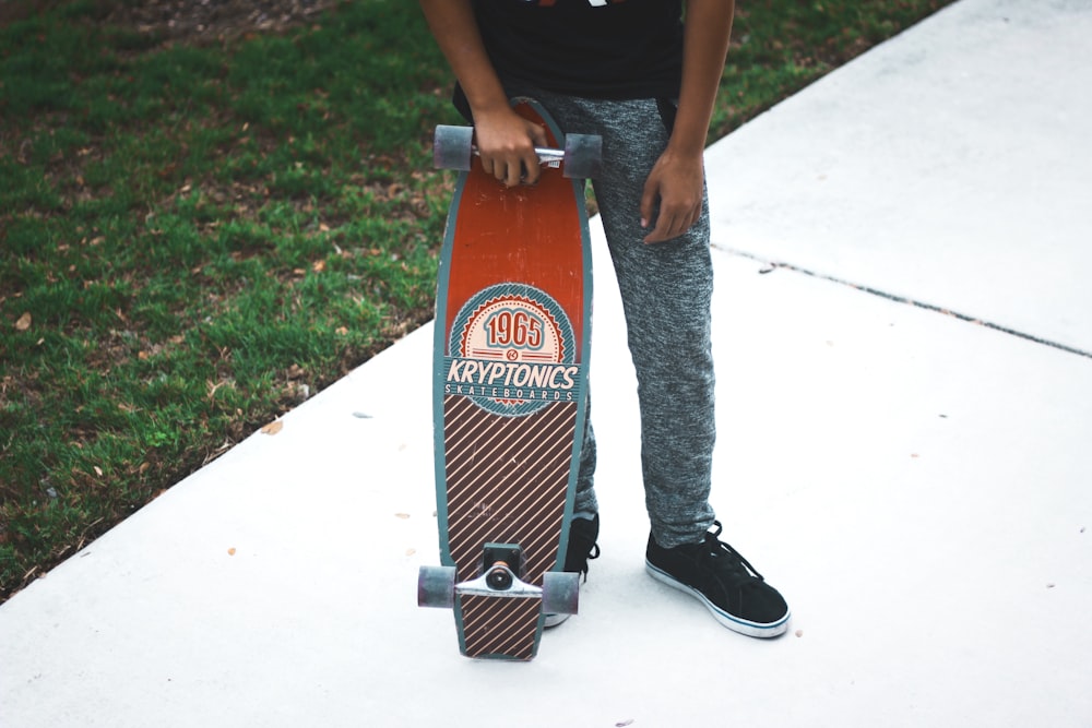 person holding red and gray Kryptonics cruiserboard standing on white tiles