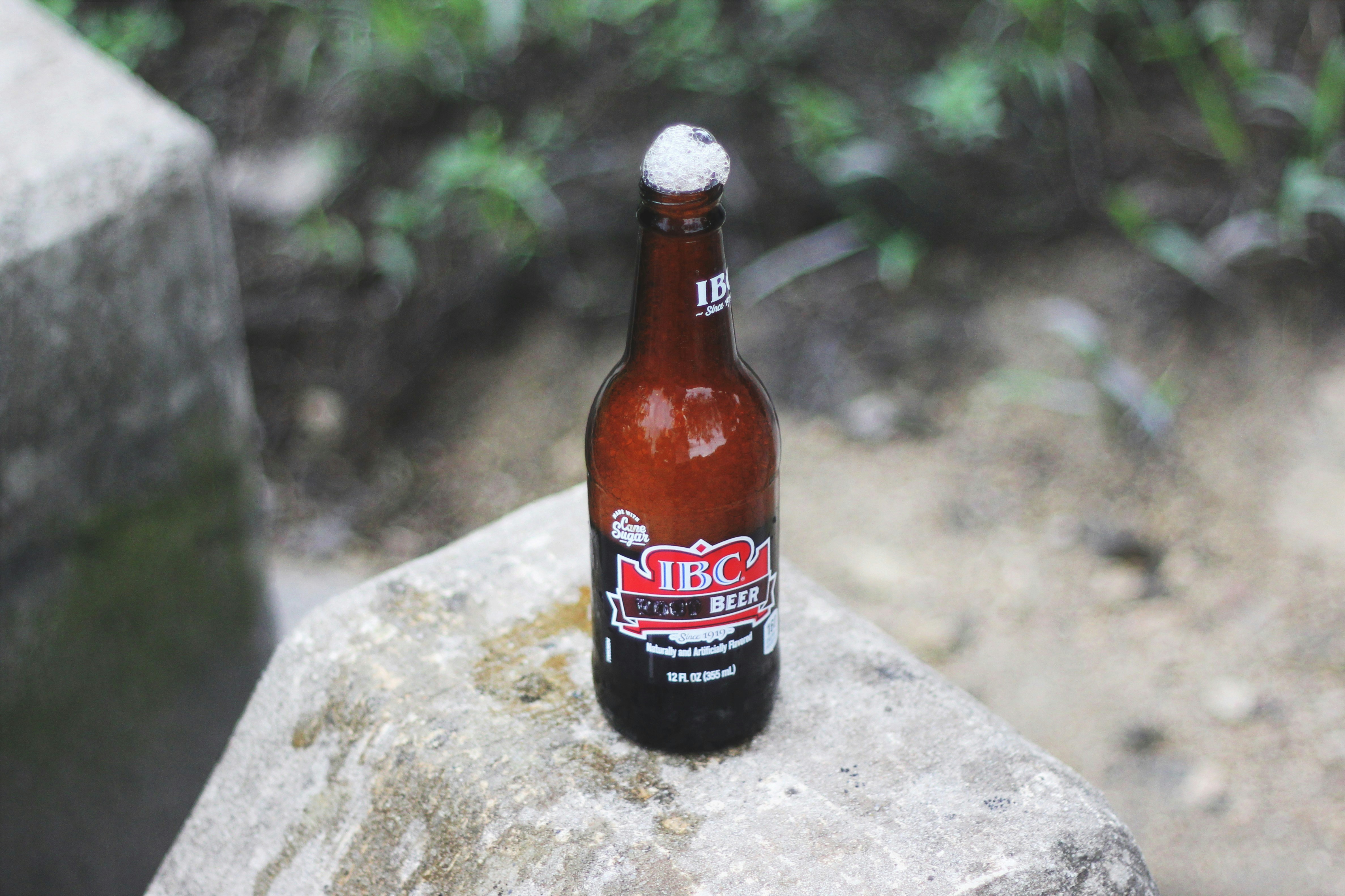 opened IBC beer bottle with foam on top on gray concrete surface during daytime