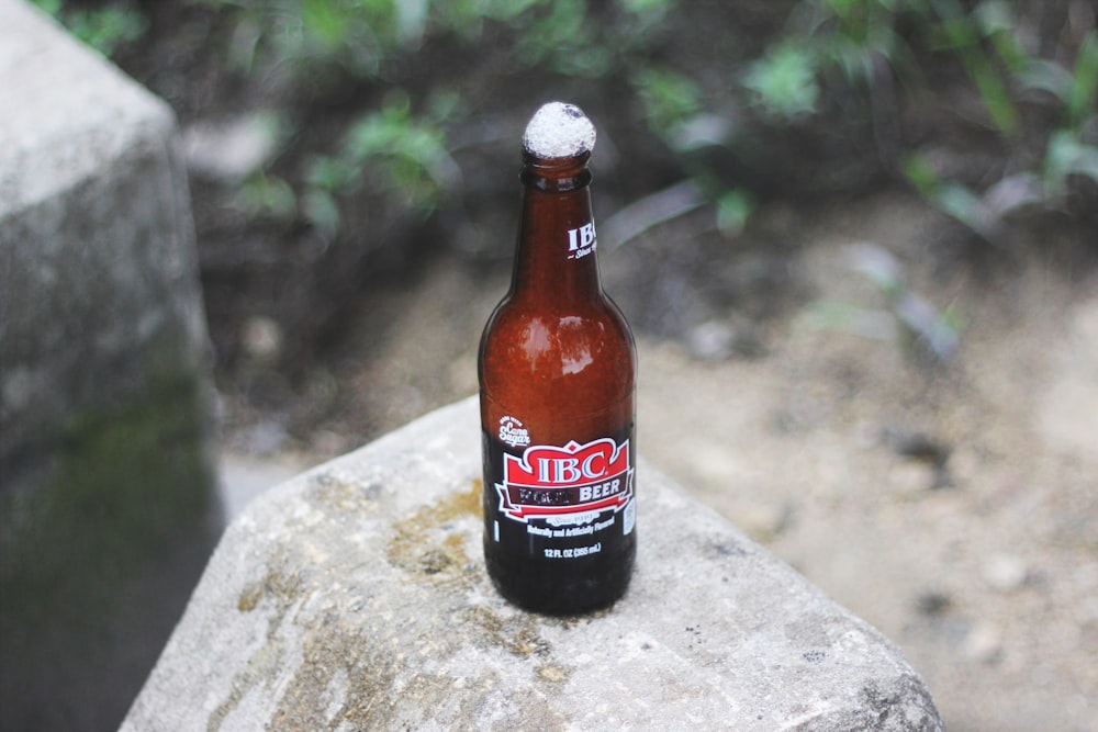 opened IBC beer bottle with foam on top on gray concrete surface during daytime