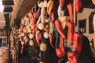 An assortment of dried chilies and other produce hanging from the ceiling of a market stall. The stall is decorated with wooden beams and mirrors on the walls. A variety of other colorful objects and trinkets are visible in the background.