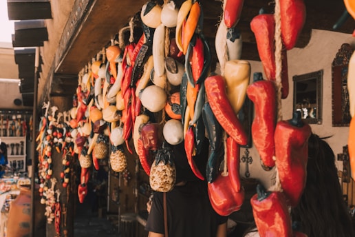 An assortment of dried chilies and other produce hanging from the ceiling of a market stall. The stall is decorated with wooden beams and mirrors on the walls. A variety of other colorful objects and trinkets are visible in the background.