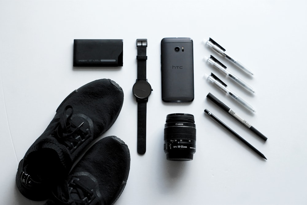 smartphone Android HTC nero accanto all'obiettivo della fotocamera, alle penne a sfera e alle scarpe stringate