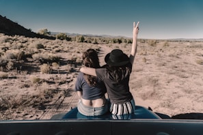 two woman sitting on car hood