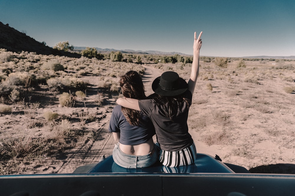 duas mulheres sentadas no capô do carro