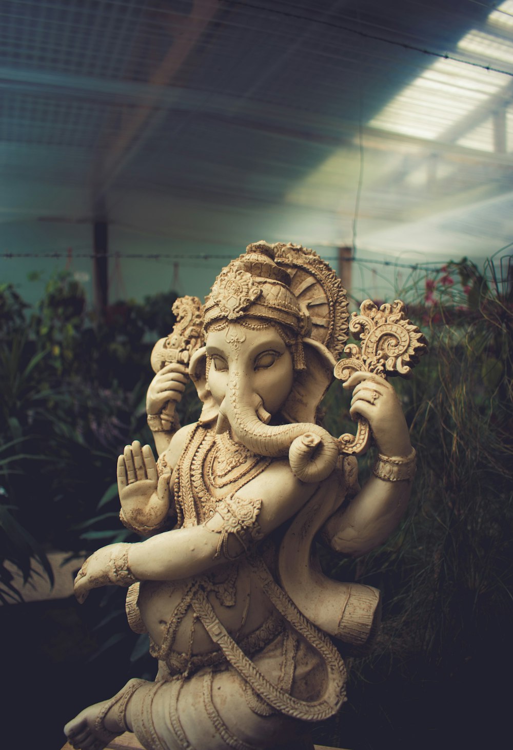 Ganesha-Statue aus braunem Beton, die hinter den Pflanzen steht