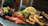 A dish featuring a variety of foods is elegantly arranged on a dark slate surface. The arrangement includes fresh green leafy lettuce, thinly sliced salmon, cucumber slices, golden fried calamari, and small fried fish. A lemon wedge provides a hint of citrus freshness.