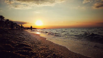 A serene beach at sunset with gentle waves and a few people walking along the shore.