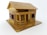 A small, intricately crafted wooden model house with a pitched roof and a porch. The structure includes windows with visible frames, and the overall design appears detailed, reflecting careful craftsmanship.