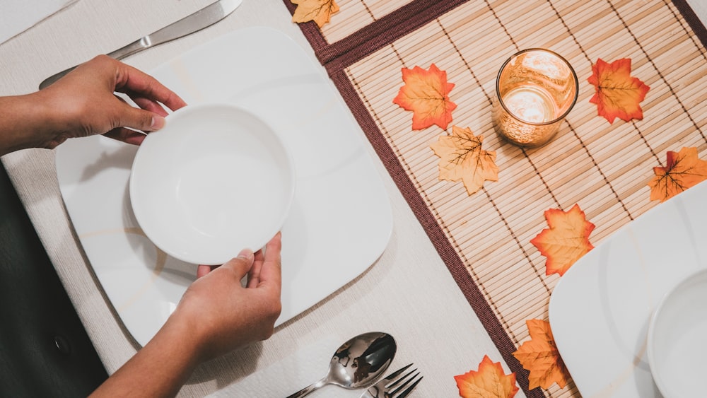 person holding round white ceramic bowl on square white ceramic plate