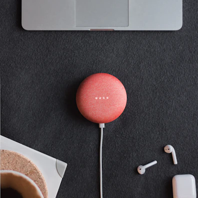 Compact smart speaker and noise-cancelling headphones resting beside a notebook and pen on a smooth black surface.