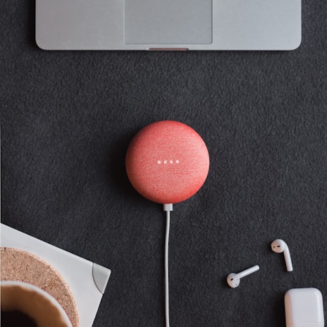 Top view of a compact pink Bluetooth speaker placed on a modern desk with tech accessories.