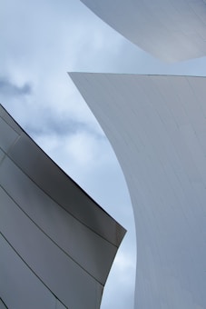 Abstract architecture with large metallic, curved surfaces set against a cloudy sky, creating a dynamic and modern aesthetic with sleek lines and subtle reflections.