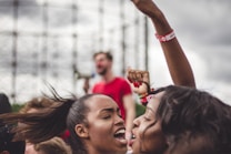 People appear to be in a celebratory or protest setting, with expressions of joy and enthusiasm. One person is in the background holding a megaphone, and two individuals in the foreground are shown with raised fists and vibrant wristbands.