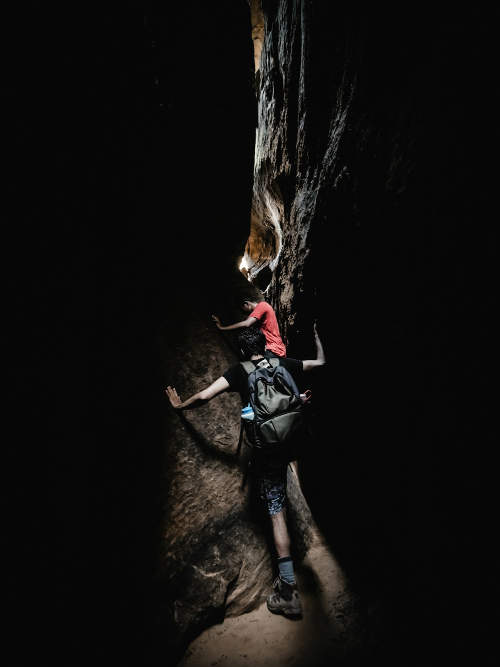 two boy's climbing between black and grey rocks during daytime