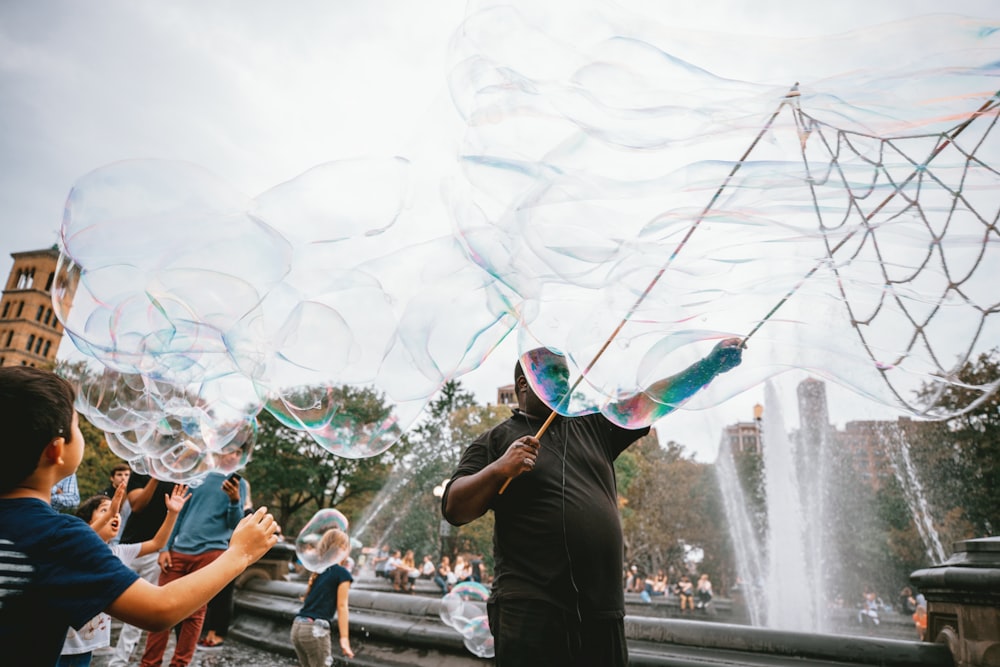 man and boy performing bubble artworks near fountain at daytime