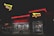 A fast-food restaurant with bright red neon signage and arrows. The building is illuminated in the night with people visible inside through large windows. The exterior has a clean and modern look, with outdoor seating and a distinctive roof design.