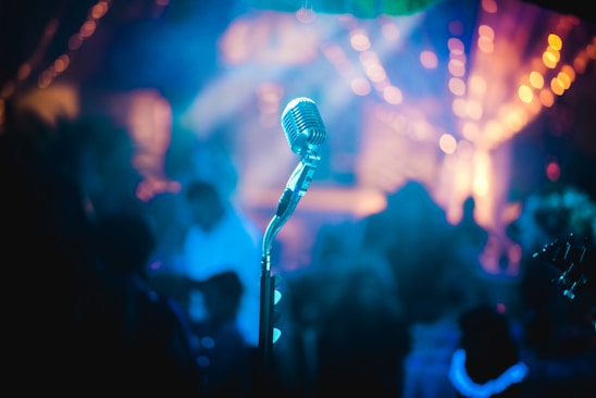 A close-up of a vintage microphone glowing under electric blue stage lights with a smoky blues club atmosphere.