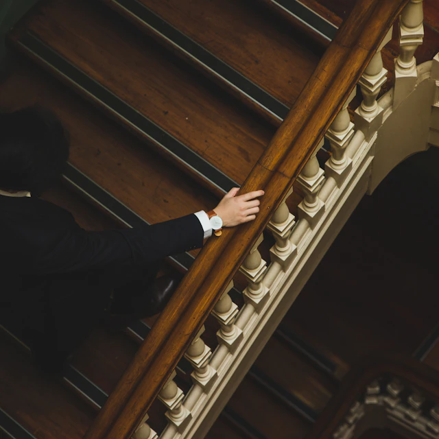 A man in a suit climbing wooden stairs with a watch on his wrist
