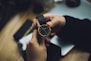 person holding gold-colored analog watch with black strap