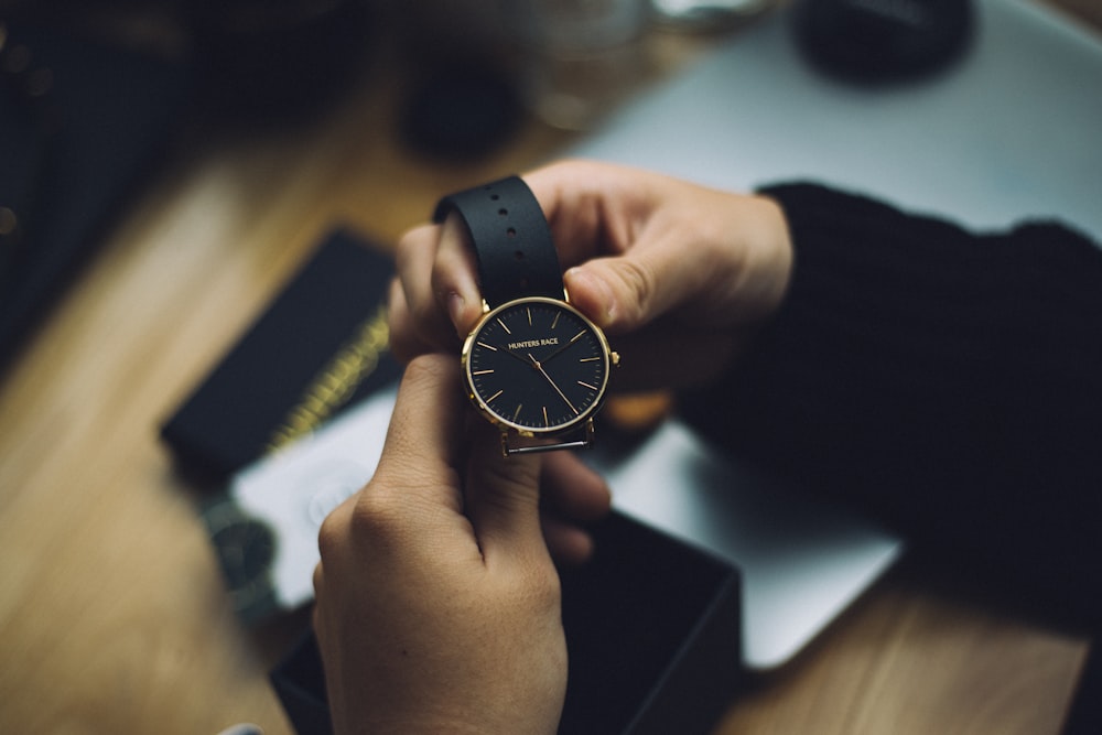 person holding gold-colored analog watch with black strap