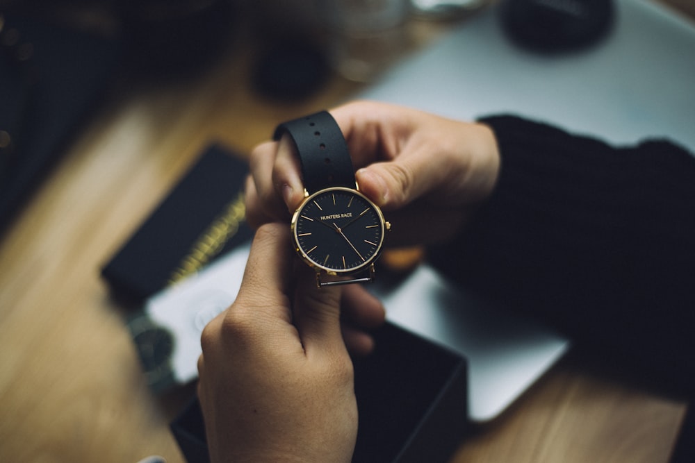 pessoa segurando relógio analógico dourado com pulseira preta