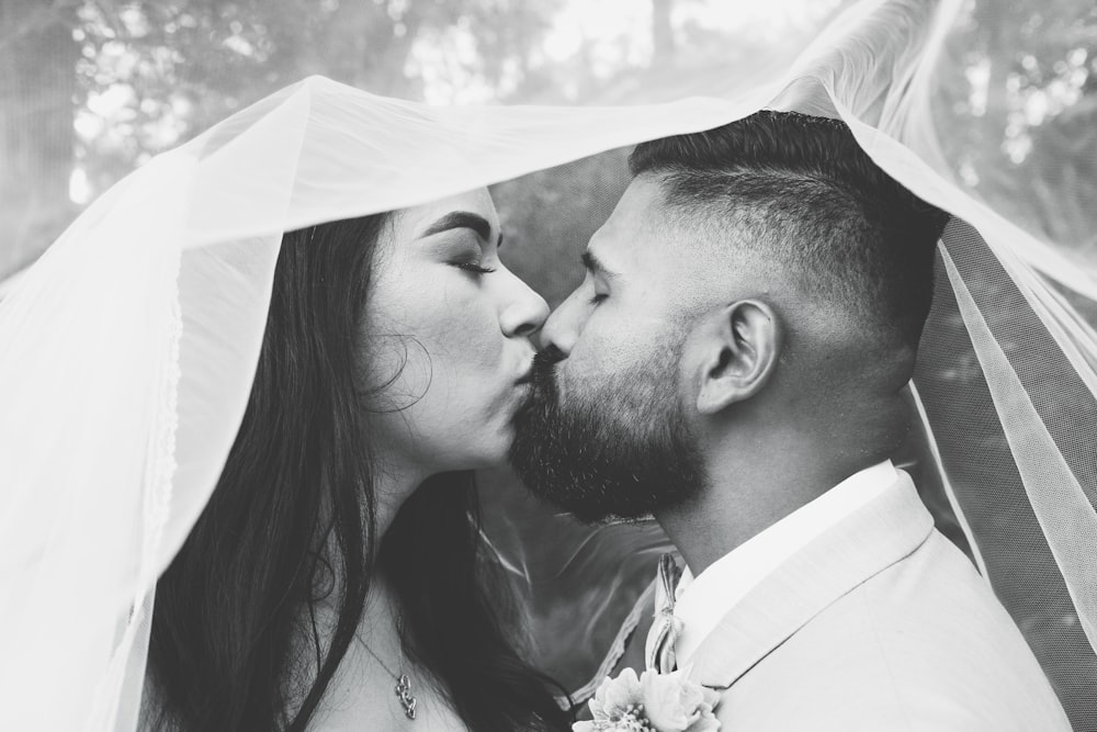 베일 아래에서 결혼한 남자와 여자의 키스하는 회색조 사진