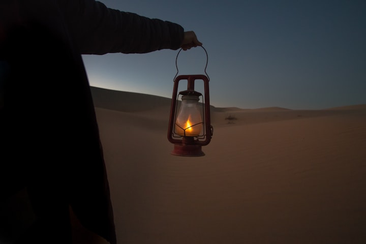 A photo of a man holding a lantern going through the desert. 