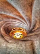 An intricate ceiling design with a central, ornate light fixture resembling a sunburst. The ceiling texture appears wavy with a honeycomb pattern, creating a dynamic swirl effect that draws the eye towards the light.
