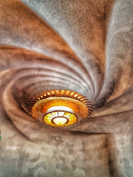 An intricate ceiling design with a central, ornate light fixture resembling a sunburst. The ceiling texture appears wavy with a honeycomb pattern, creating a dynamic swirl effect that draws the eye towards the light.