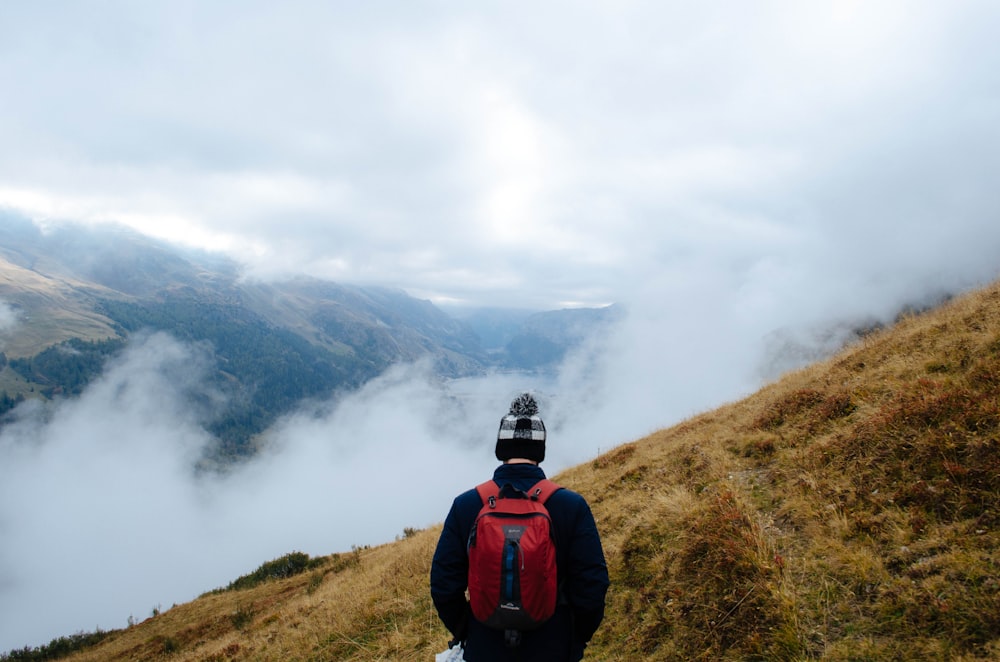 man with red backpack on top of foggy mountai n