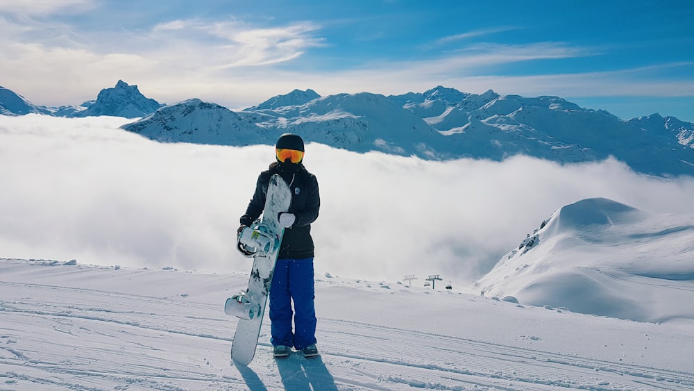 man carrying snowboard standing on snow-covered mountain