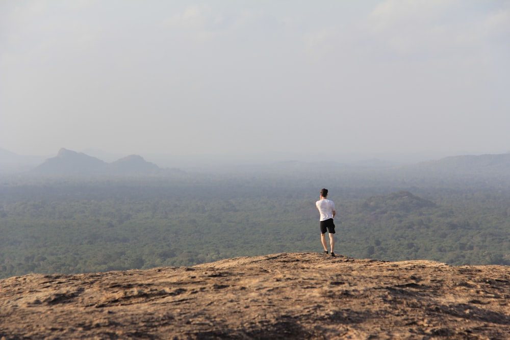 man in white T-shirt standing on mountain during day time