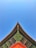A traditional Asian architectural roof corner with intricate wooden carvings and vibrant colors, set against a clear blue sky. The beams and eaves exhibit detailed craftsmanship with green, red, and golden hues.