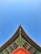 A traditional Asian architectural roof corner with intricate wooden carvings and vibrant colors, set against a clear blue sky. The beams and eaves exhibit detailed craftsmanship with green, red, and golden hues.