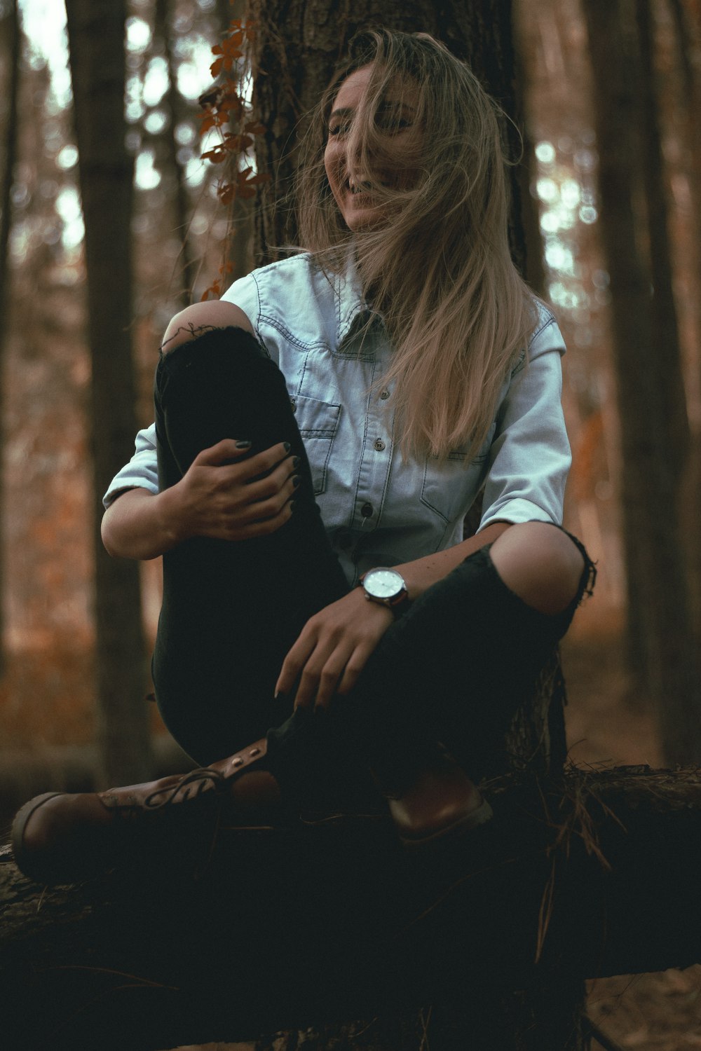 femme rieuse appuyée sur un tronc d’arbre gris