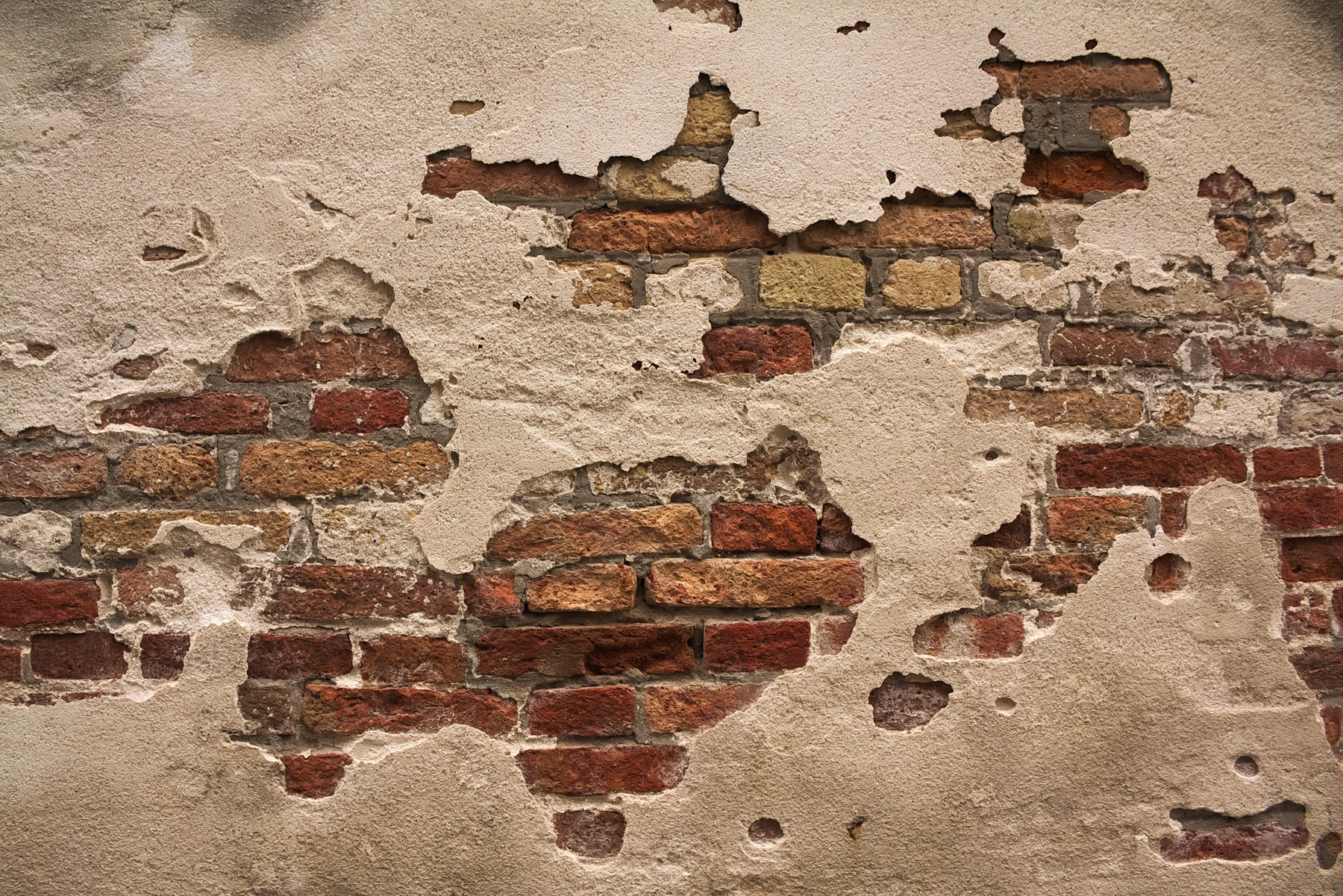 Old red brick showing through crumbling grey render
