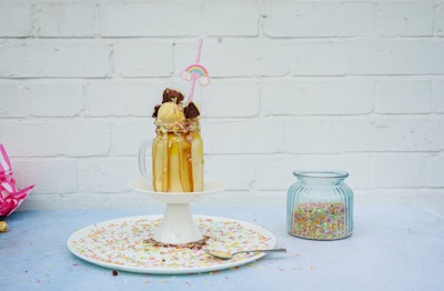 A creamy milkshake in a glass jar with a striped straw, surrounded by sprinkles.