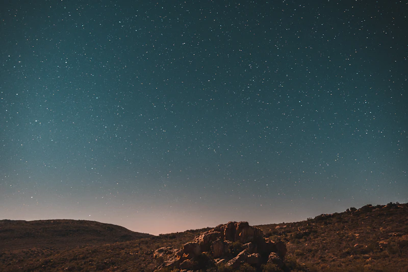 A star-filled night sky over a dark African landscape ridge