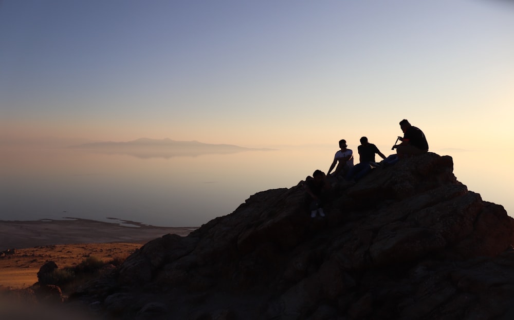 silhouette of men sitting on hill at daytime