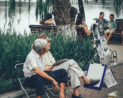 two men sitting on bench beside portrait paintings