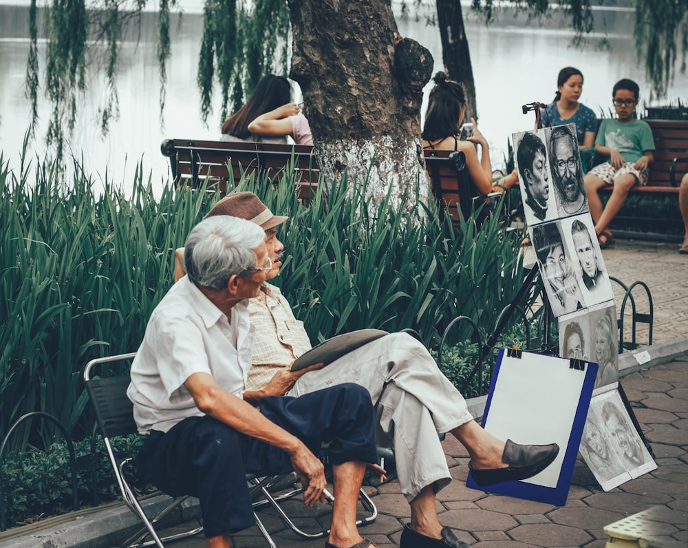 two men sitting on bench beside portrait paintings