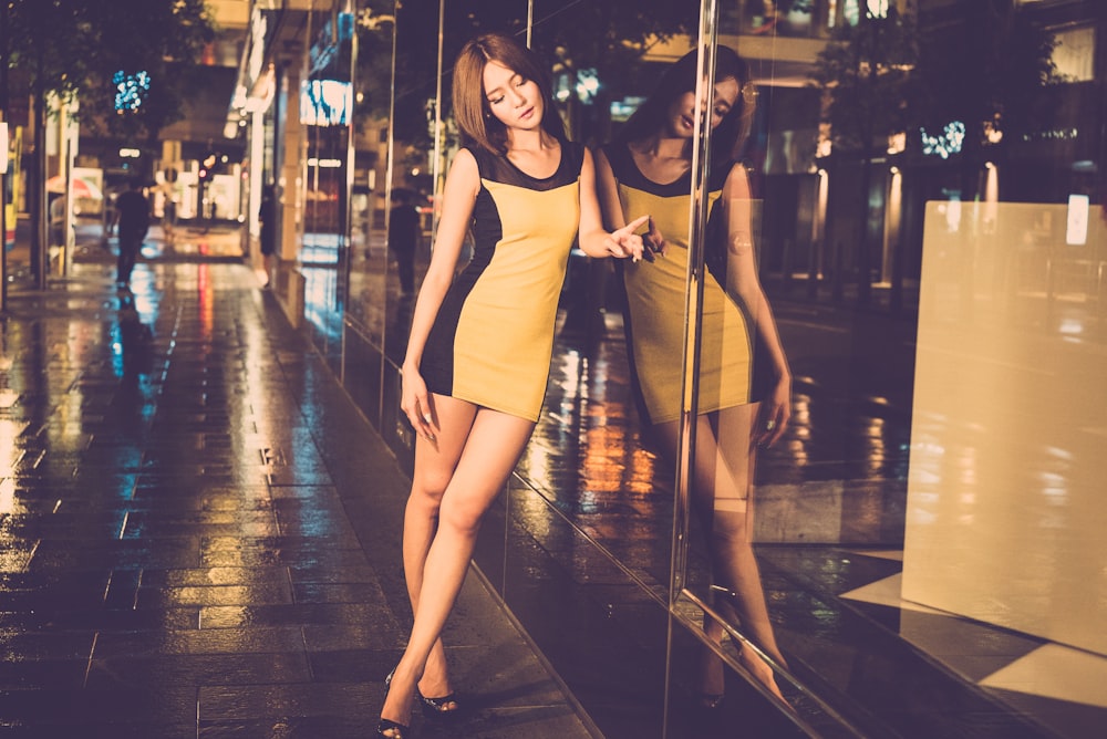 woman wearing brown and black sleeveless dress lean on glass wall