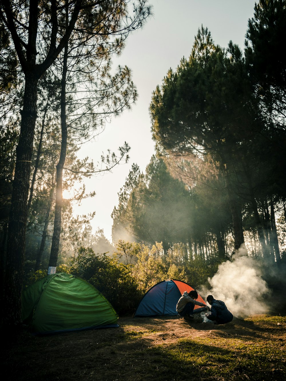 duas pessoas sentadas perto de duas barracas de acampamento na floresta
