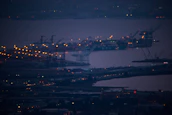 A panoramic view of a busy port at dusk, with ships docked and cranes in motion.