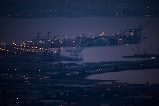 A sprawling port at dusk with cargo ships being loaded under navy and brass lighting.