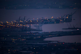 A panoramic view of a busy port at dusk, with ships docked and cranes in motion.